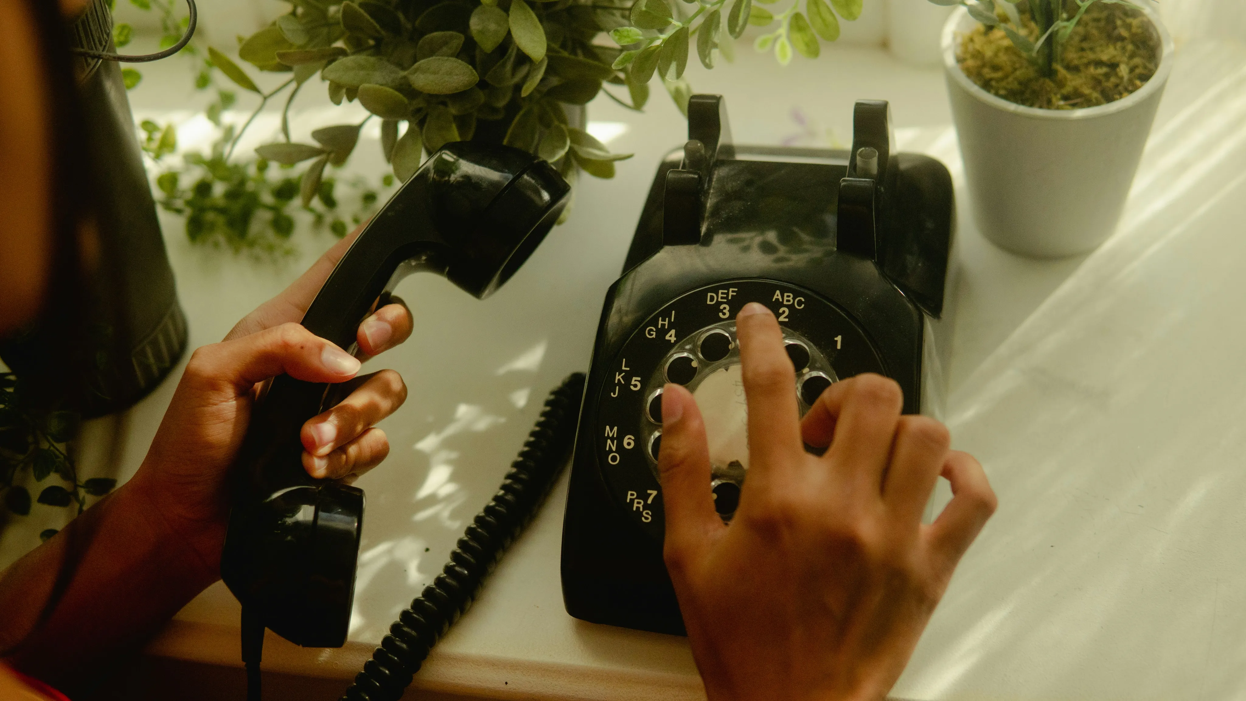 Hands dialling an old black rotary telephone.