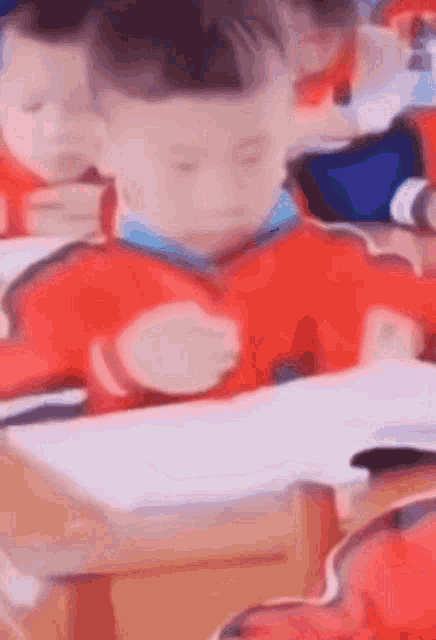 A young boy in a red jumper at a school desk, concentrating hard as he counts.